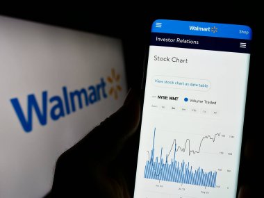 Stuttgart, Almanya - 08-13-2023: ABD 'li perakende şirketi Walmart Inc.' in web sayfası ile akıllı telefonu olan kişi iş logosu önünde ekranda. Telefon ekranının merkezine odaklan.