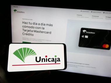 Stuttgart, Almanya - 08-13-2023: İspanyol bankacılık şirketi Unicaja Banco S.A. 'nın logosunun bulunduğu cep telefonu web sayfası önünde ekranda. Telefon ekranına odaklan.