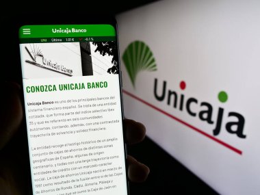 Stuttgart, Almanya - 08-13-2023: İspanyol bankacılık şirketi Unicaja Banco S.A. 'nın internet sitesiyle cep telefonu tutan kişi logolu ekranda. Telefon ekranının merkezine odaklan.