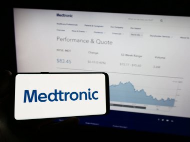 Stuttgart, Almanya - 08-14-2023: Medikal teknoloji şirketi Medtronic plc 'in logosuna sahip cep telefonu sahibi kişi iş sayfasının önünde ekranda. Telefon ekranına odaklan.