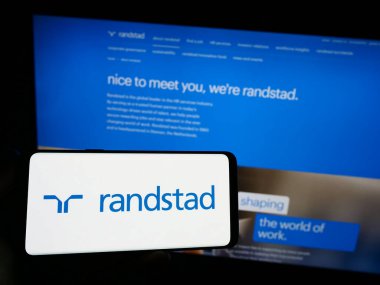 Stuttgart, Almanya - 08-14-2023: Hollandalı insan kaynakları şirketi Randstad NV 'nin logosuna sahip akıllı telefon sahibi kişi web sitesinin önünde ekranda. Telefon ekranına odaklan.
