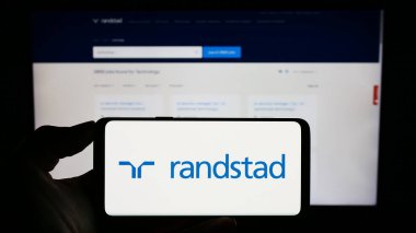 Stuttgart, Almanya - 08-14-2023: Hollandalı insan kaynakları şirketi Randstad N.V. 'nin logosuyla cep telefonu sahibi kişi iş sayfasının önünde ekranda. Telefon ekranına odaklan.