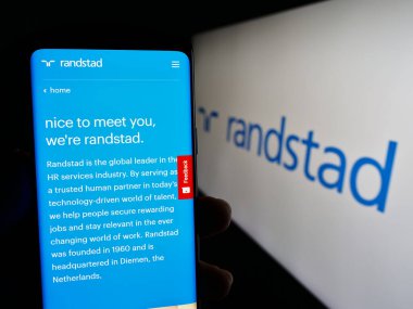 Stuttgart, Almanya - 08-14-2023: Hollandalı insan kaynakları şirketi Randstad N.V. 'nin internet sayfası ile cep telefonu tutan kişi logolu ekranda. Telefon ekranının merkezine odaklan.