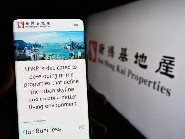 Stuttgart, Almanya - 08-14-2023: Sun Hung Kai Properties Limited (SHKP) şirketinin web sayfasını elinde tutan kişi ekranda logolu. Telefon ekranının merkezine odaklan.