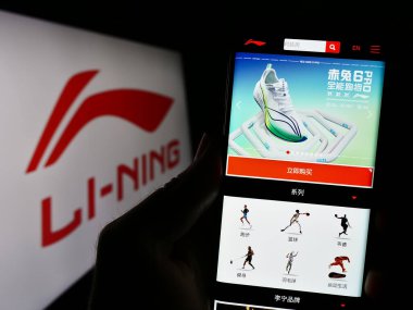 Stuttgart, Germany - 08-15-2023: Person holding cellphone with website of Chinese company Li-Ning Company Limited on screen in front of logo. Focus on center of phone display. clipart