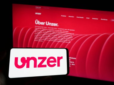 Stuttgart, Almanya - 08-15-2023: Alman ödeme şirketi Unzer GmbH 'nin logosunun bulunduğu cep telefonu sahibi kişi iş sayfasının önünde ekranda. Telefon ekranına odaklan.