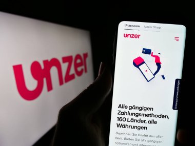 Stuttgart, Almanya - 08-15-2023: Alman ödeme şirketi Unzer GmbH 'nin web sitesi ile cep telefonu elinde bulunan kişi logonun önünde ekranda. Telefon ekranının merkezine odaklan.