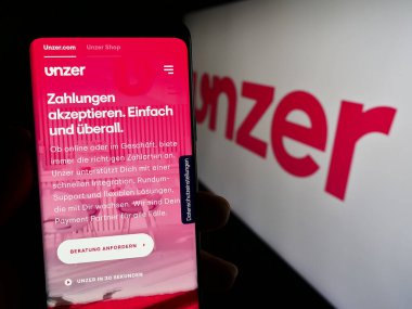 Stuttgart, Almanya - 08-15-2023: Alman ödeme şirketi Unzer GmbH 'nin web sitesi ile cep telefonu elinde tutan kişi logonun önünde ekranda. Telefon ekranının merkezine odaklan.