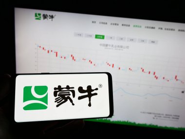 Stuttgart, Almanya - 08-16-2023: Çinli Mengniu Dairy Company 'nin logosunun bulunduğu cep telefonu sahibi kişi iş sayfasının önünde ekranda. Telefon ekranına odaklan.