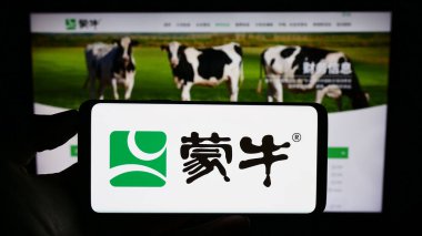 Stuttgart, Almanya - 08-16-2023: Çin Mengniu Dairy Company 'nin logosunun bulunduğu akıllı telefon sahibi kişi web sitesinin önünde ekranda. Telefon ekranına odaklan.