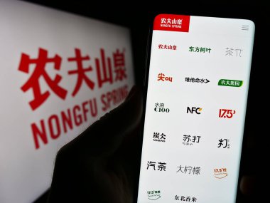 Stuttgart, Germany - 08-16-2023: Person holding cellphone with webpage of Chinese business Nongfu Spring Company Limited on screen with logo. Focus on center of phone display. clipart