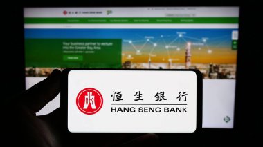 Stuttgart, Almanya - 08-16-2023: Çinli şirket Hang Seng Bank Limited 'in logosuna sahip akıllı telefon sahibi kişi web sitesinin önünde ekranda. Telefon ekranına odaklan.