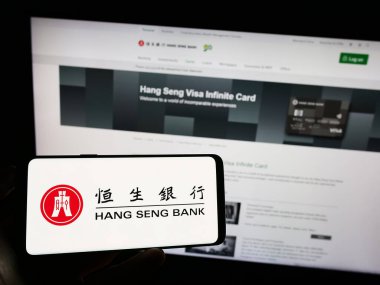Stuttgart, Almanya - 08-16-2023: Çinli şirket Hang Seng Bank Limited 'in logosuyla cep telefonu sahibi kişi iş sayfasının önünde ekranda. Telefon ekranına odaklan.