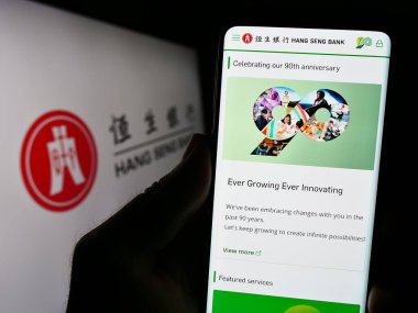 Stuttgart, Almanya - 08-16-2023: Çinli şirket Hang Seng Bank Limited 'in web sitesi ile akıllı telefon sahibi kişi logonun önünde ekranda. Telefon ekranının merkezine odaklan.