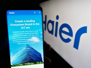 Stuttgart, Almanya - 08-17-2023: Ev aletleri şirketi Haier Group Corporation 'ın web sayfası ile cep telefonu tutan kişi logolu ekranda. Telefon ekranının merkezine odaklan.