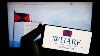 Stuttgart, Almanya - 08-17-2023: Çinli şirket The Wharf Holding Limited 'in logosunun bulunduğu akıllı telefon sahibi kişi web sitesinin önünde ekranda. Telefon ekranına odaklan.