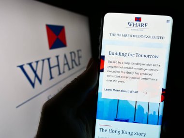 Stuttgart, Almanya - 08-17-2023: Çinli şirket The Wharf Holdings Limited 'in web sayfası ile cep telefonu tutan kişi logonun önünde ekranda görülüyor. Telefon ekranının merkezine odaklan.