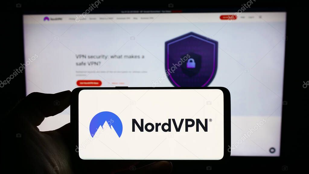 Stuttgart, Germany - 08-17-2023: Person holding cellphone with logo of VPN service NordVPN (Nordsec Ltd.) on screen in front of business webpage. Focus on phone display.