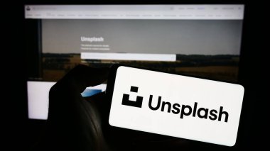 Stuttgart, Almanya - 08-18-2023: Stok fotoğrafçılık şirketi Unsplash Inc. 'in logosunun bulunduğu cep telefonu sahibi kişi iş sayfasının önünde ekranda. Telefon ekranına odaklan.