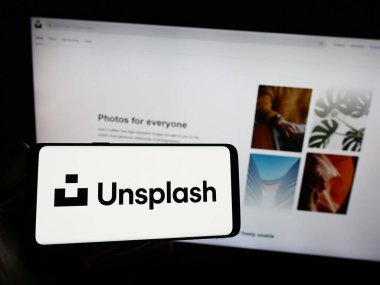 Stuttgart, Almanya - 08-18-2023: Stok fotoğrafçılık şirketi Unsplash Inc. 'in logosuna sahip akıllı telefon sahibi kişi web sitesinin önünde ekranda. Telefon ekranına odaklan.