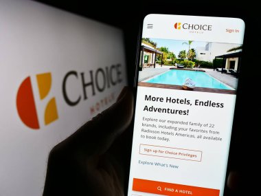 Stuttgart, Germany - 08-18-2023: Person holding cellphone with website of US company Choice Hotels International Inc. on screen in front of logo. Focus on center of phone display. clipart