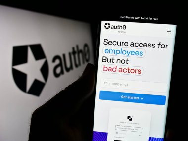 Stuttgart, Germany - 08-20-2023: Person holding cellphone with webpage of US identity platform company Auth0 by Okta on screen in front of logo. Focus on center of phone display. clipart