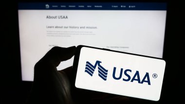 Stuttgart, Almanya - 08-20-2023: Birleşik Hizmetler Otomobil Birliği 'nin (USAA) logosuna sahip akıllı telefonu web sitesi önünde ekranda tutan kişi. Telefon ekranına odaklan.