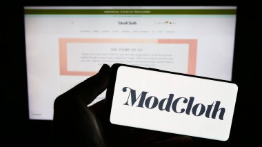 Stuttgart, Germany - 08-20-2023: Person holding smartphone with logo of US e-commerce company ModCloth on screen in front of website. Focus on phone display. clipart