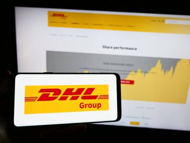 Stuttgart, Almanya - 08-20-2023: İnternet sayfası önünde üzerinde lojistik şirketi Deutsche Post (DHL Group) logosu bulunan cep telefonu sahibi kişi. Telefon ekranına odaklan.