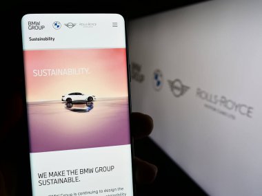 Stuttgart, Almanya - 08-20-2023: Bayerische Motoren Werke AG (BMW Group) şirketinin web sayfası ile akıllı telefon sahibi kişi logo ile ekranda. Telefon ekranının merkezine odaklan.