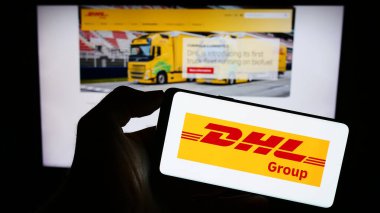 Stuttgart, Almanya - 08-20-2023: İnternet sayfası önünde üzerinde lojistik şirketi Deutsche Post (DHL Group) logosu bulunan cep telefonu sahibi kişi. Telefon ekranına odaklan.