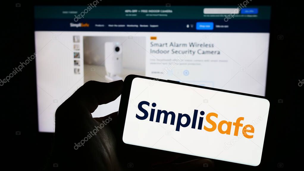Stuttgart, Germany - 08-20-2023: Person holding cellphone with logo of US home security company SimpliSafe Inc. on screen in front of business webpage. Focus on phone display.