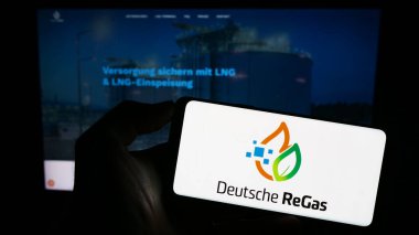 Stuttgart, Almanya - 08-20-2023: Alman firması Deutsche ReGas GmbH Co. KGaA 'nın logosuyla cep telefonu sahibi kişi iş sayfası önünde ekranda. Telefon ekranına odaklan.