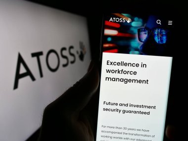 Stuttgart, Almanya - 08-20-2023: İşgücü yönetim şirketi Atoss Software AG 'nin web sayfası ile akıllı telefon taşıyan kişi logolu ekranda. Telefon ekranının merkezine odaklan.