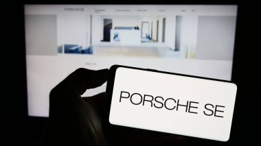 Stuttgart, Almanya - 08-20-2023: Alman şirketi Porsche Automobil Holding SE 'nin logosunu elinde tutan kişi web sitesinin önünde ekranda. Telefon ekranına odaklan.