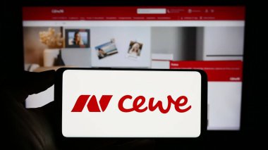 Stuttgart, Almanya - 08-21-2023: Baskı şirketi CEWE Stiftung Co. KGaA 'nın logosuyla cep telefonu sahibi kişi iş sayfası önünde ekranda. Telefon ekranına odaklan.