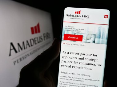 Stuttgart, Almanya - 08-21-2023: Alman işe alım şirketi Amadeus FiRe AG 'nin web sitesi ile cep telefonu tutan kişi logo önünde ekranda görülüyor. Telefon ekranının merkezine odaklan.
