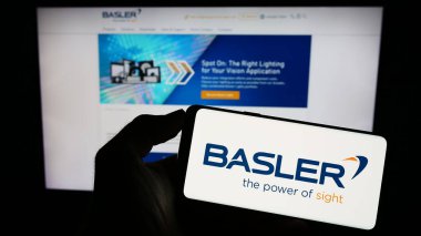 Stuttgart, Germany - 08-21-2023: Person holding cellphone with logo of German imaging company Basler AG on screen in front of business webpage. Focus on phone display. clipart