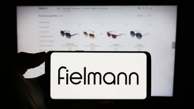 Stuttgart, Almanya - 08-21-2023: Alman gözlük şirketi Fielmann AG 'nin logosuyla cep telefonu tutan kişi iş sayfasının önünde ekranda. Telefon ekranına odaklan.