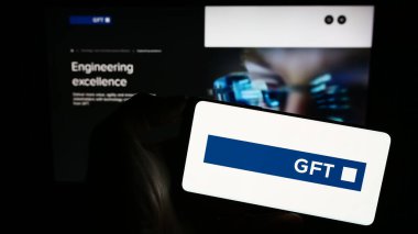 Stuttgart, Almanya - 08-21-2023: Alman bilişim şirketi GFT Technologies SE 'nin logosuyla cep telefonu sahibi kişi iş sayfası önünde ekranda. Telefon ekranına odaklan.