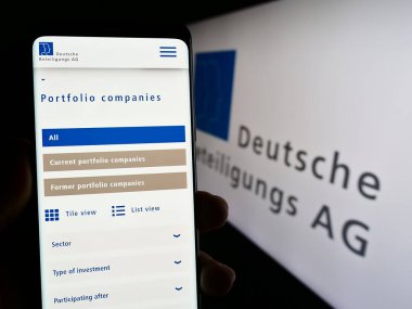Stuttgart, Almanya - 08-21-2023: Alman firması Deutsche Beteiligungs AG 'nin (DBAG) web sayfası ile cep telefonu tutan kişi logo ile ekranda. Telefon ekranının merkezine odaklan.