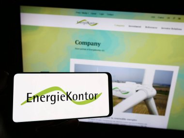 Stuttgart, Germany - 08-21-2023: Person holding smartphone with logo of German renewable energy company Energiekontor AG on screen in front of website. Focus on phone display. clipart