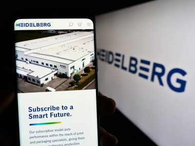 Stuttgart, Almanya - 08-22-2023: Alman şirketi Heidelberger Druckmaschinen AG 'nin web sitesi ile akıllı telefonu elinde tutan kişi logolu ekranda. Telefon ekranının merkezine odaklan.