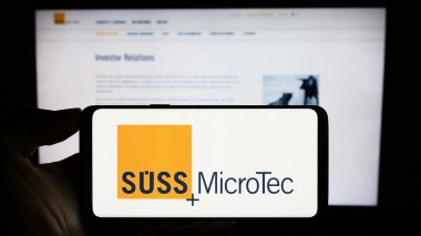 Stuttgart, Germany - 08-22-2023: Person holding cellphone with logo of German technology company Suss Microtec SE on screen in front of business webpage. Focus on phone display. clipart