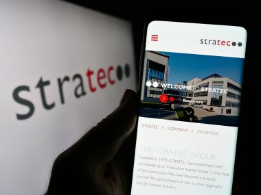 Stuttgart, Almanya - 08-22-2023: Alman tanı firması STRATEC SE 'nin web sitesi ile birlikte logo önünde cep telefonu tutan kişi. Telefon ekranının merkezine odaklan.