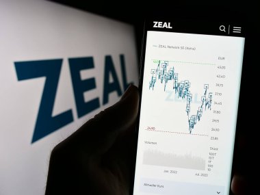 Stuttgart, Almanya - 08-24-2023: Logo önündeki ekranda Alman piyango şirketi ZEAL Network SE 'nin web sayfası ile cep telefonu tutan kişi. Telefon ekranının merkezine odaklan.