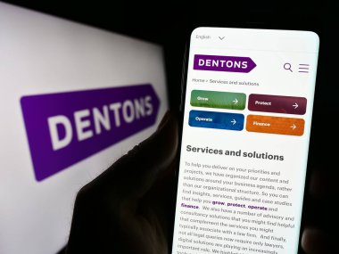 Stuttgart, Almanya - 08-24-2023: Küresel hukuk şirketi Dentons 'un web sitesi ile akıllı telefonu olan kişi iş logosu önünde ekranda. Telefon ekranının merkezine odaklan.