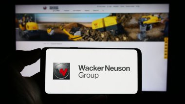 Stuttgart, Almanya - 08-24-2023: Alman makine şirketi Wacker Neuson SE 'nin logosunu elinde tutan kişi iş sayfasının önünde ekranda. Telefon ekranına odaklan.