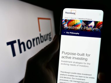 Stuttgart, Almanya - 08-25-2023: Thornburg Investment Management Inc. 'nin web sitesi ile cep telefonu elinde tutan kişi logo ile ekranda. Telefon ekranının merkezine odaklan.