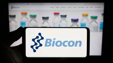Stuttgart, Almanya - 08-26-2023: Hint biyofarmasötik şirketi Biocon Limited 'in logosuna sahip akıllı telefon sahibi kişi web sitesinin önünde ekranda. Telefon ekranına odaklan.